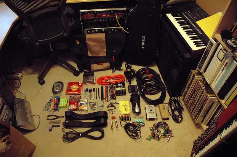A gig bag with its contents laid out on the floor: cables, an extension cord, pens, batteries and tools