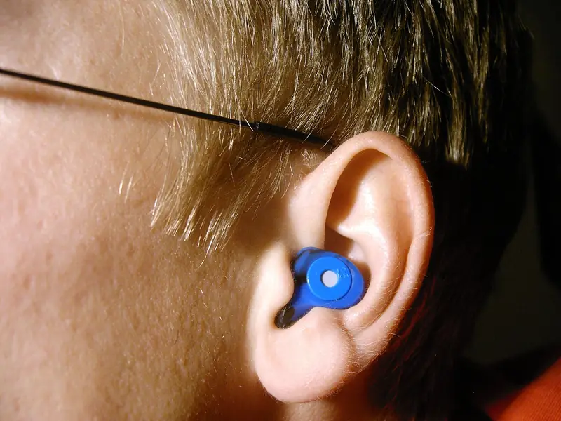 Close-up of an ear wearing a blue custom-molded silicone earplug with a round filter in its center