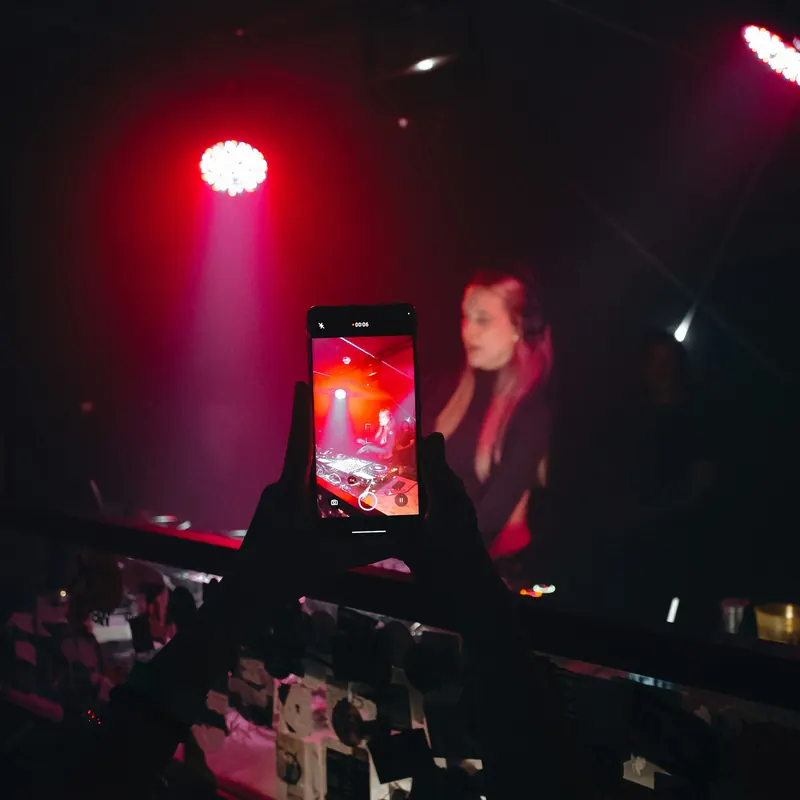 Hands holding up a phone that films a DJ playing under red club lights