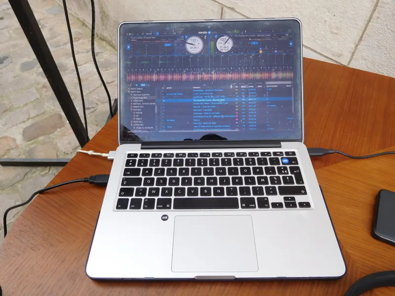 Laptop running Serato DJ Pro with two virtual decks, waveforms and a track list on screen