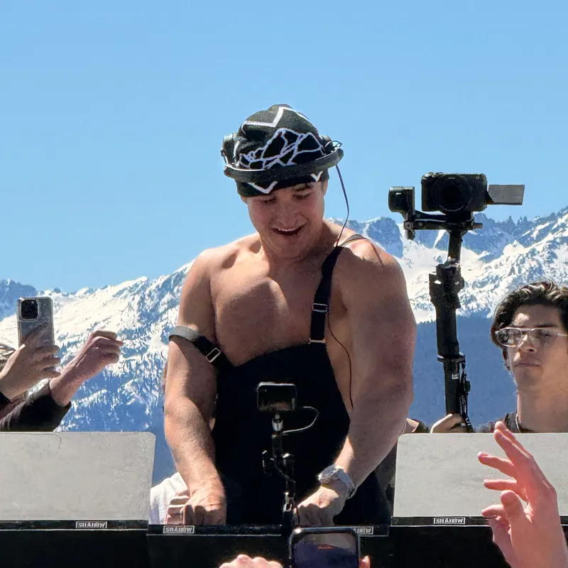 John Summit at the decks on an outdoor stage, with snowy mountains behind him